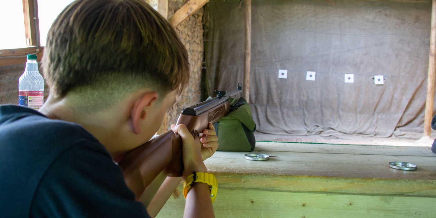 Child aims an air rifle within a shooting range.