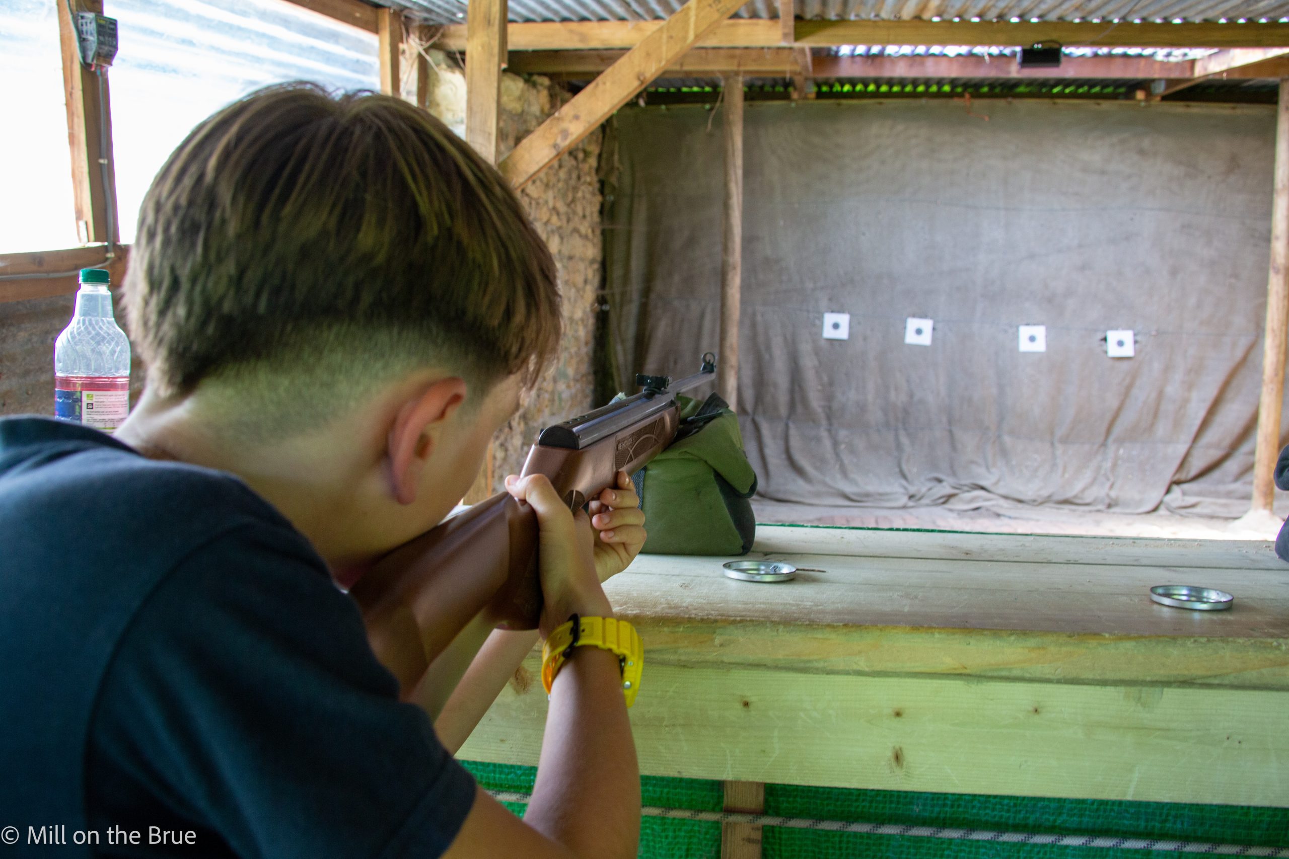 Child aims an air rifle within a shooting range.