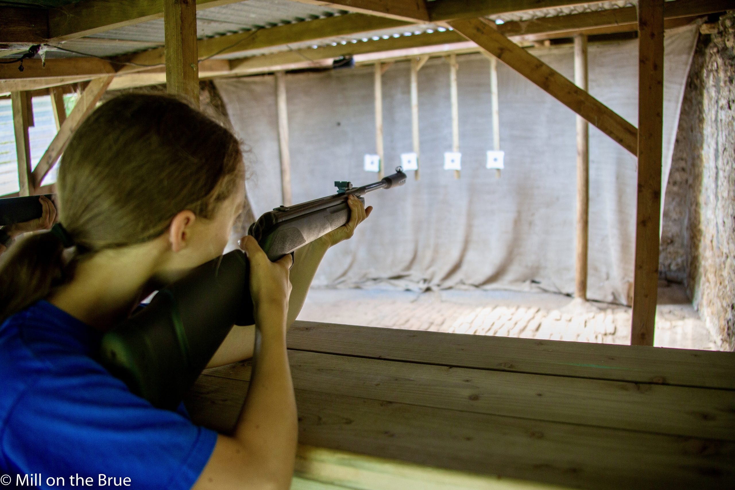 Child aims an air rifle within a shooting range.