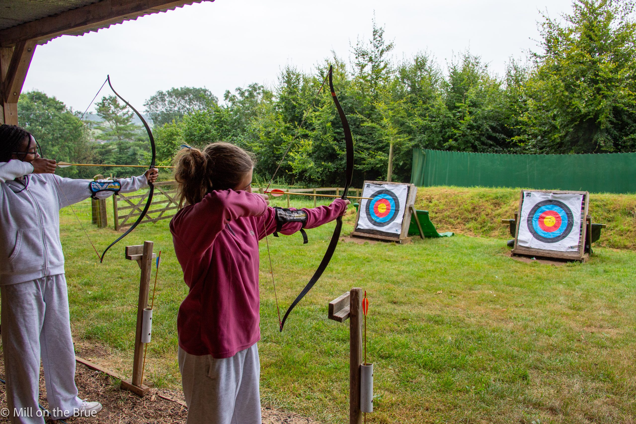 Students aim bows and arrows at archery targets.