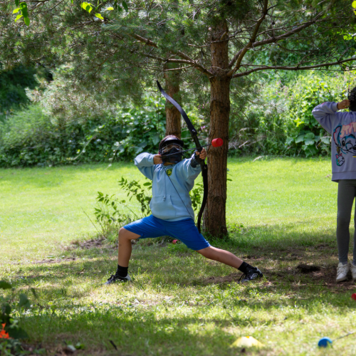 A child with legs stretched out about to shoot an arrow in archery tag