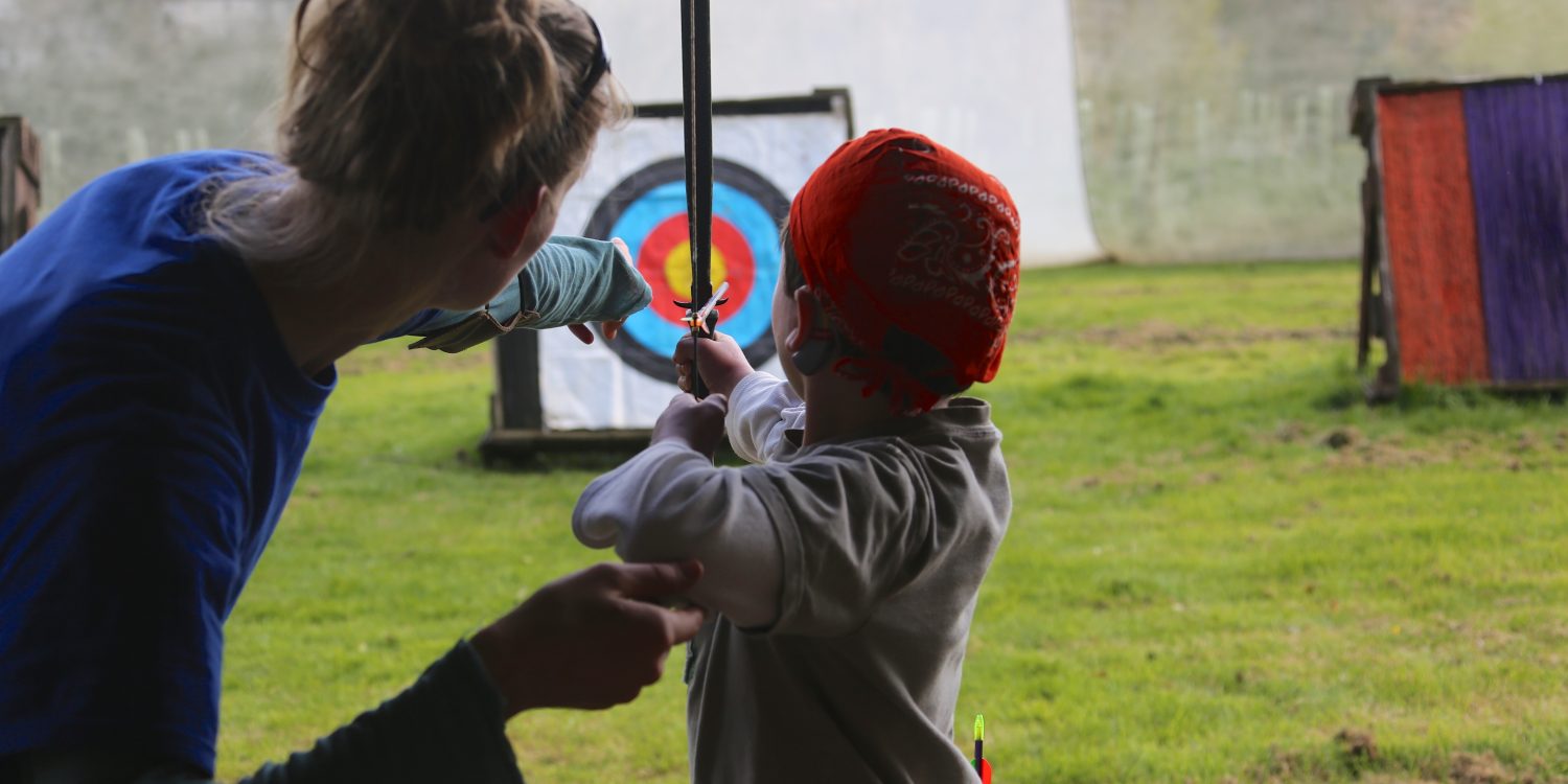 Instructor helps a child aim a bow.