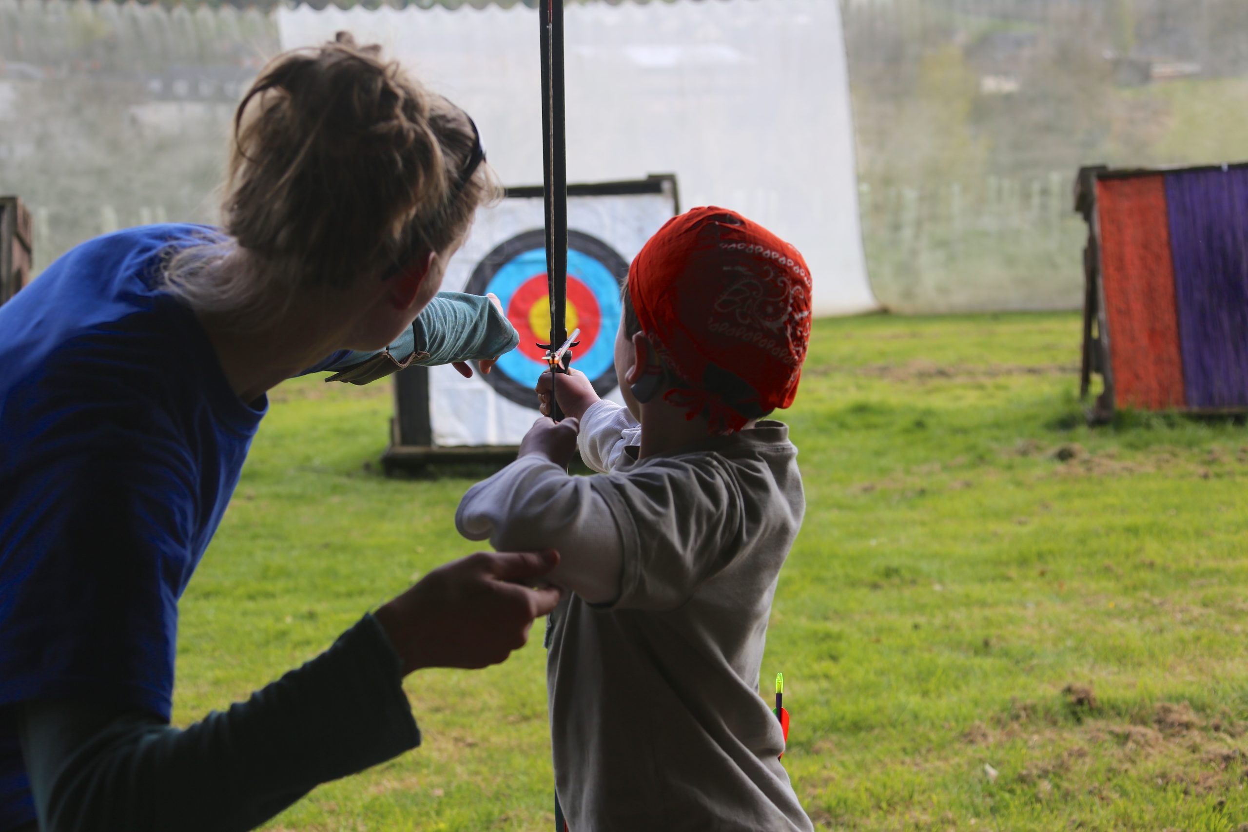 Instructor helps a child aim a bow.