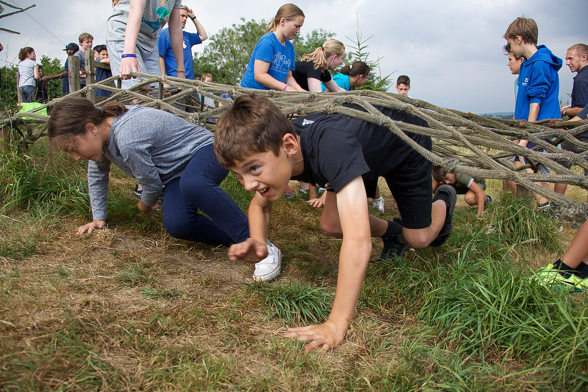 Children army crawl under a net.