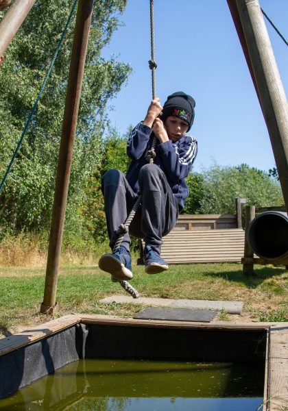 Child swings on a rope over water.