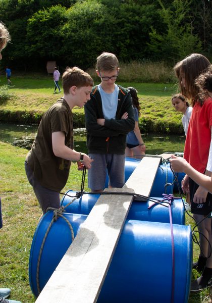 Students build a bridge of barrels, planks, and rope.