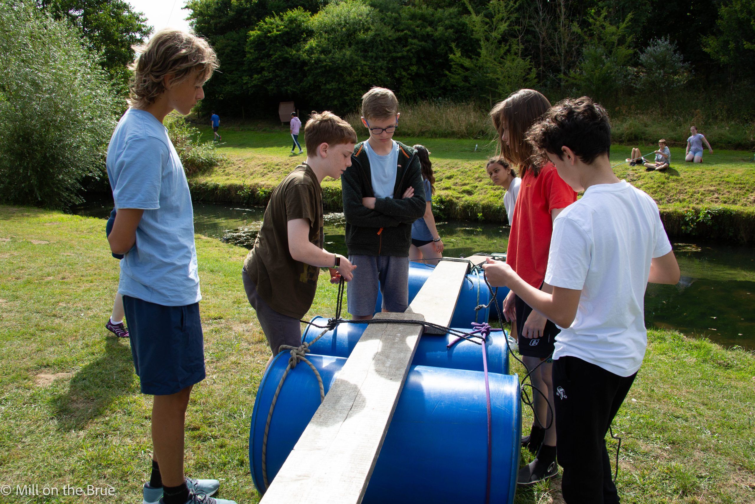 Students build a bridge of barrels, planks, and rope.