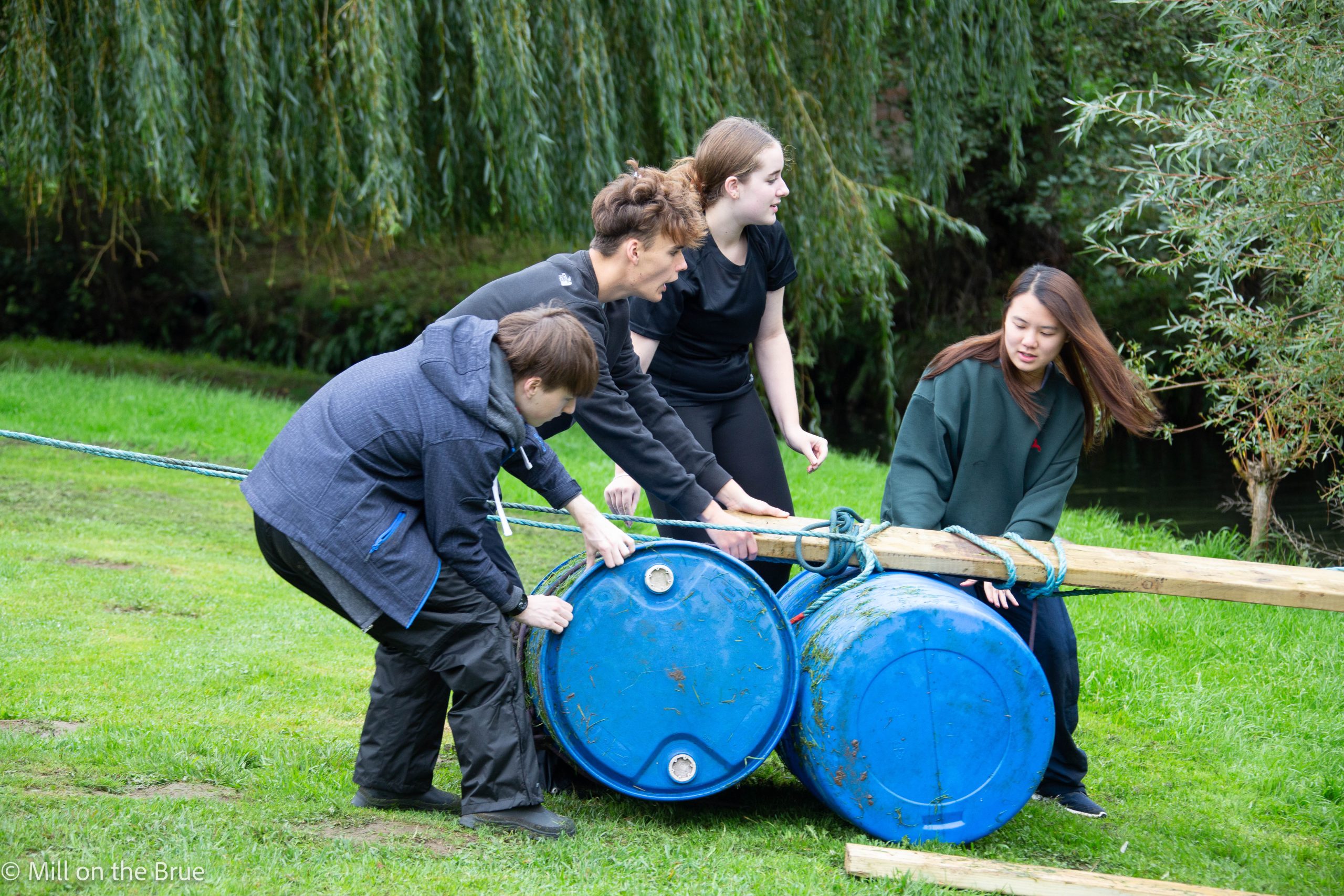 Students build a bridge of barrels, planks, and rope.