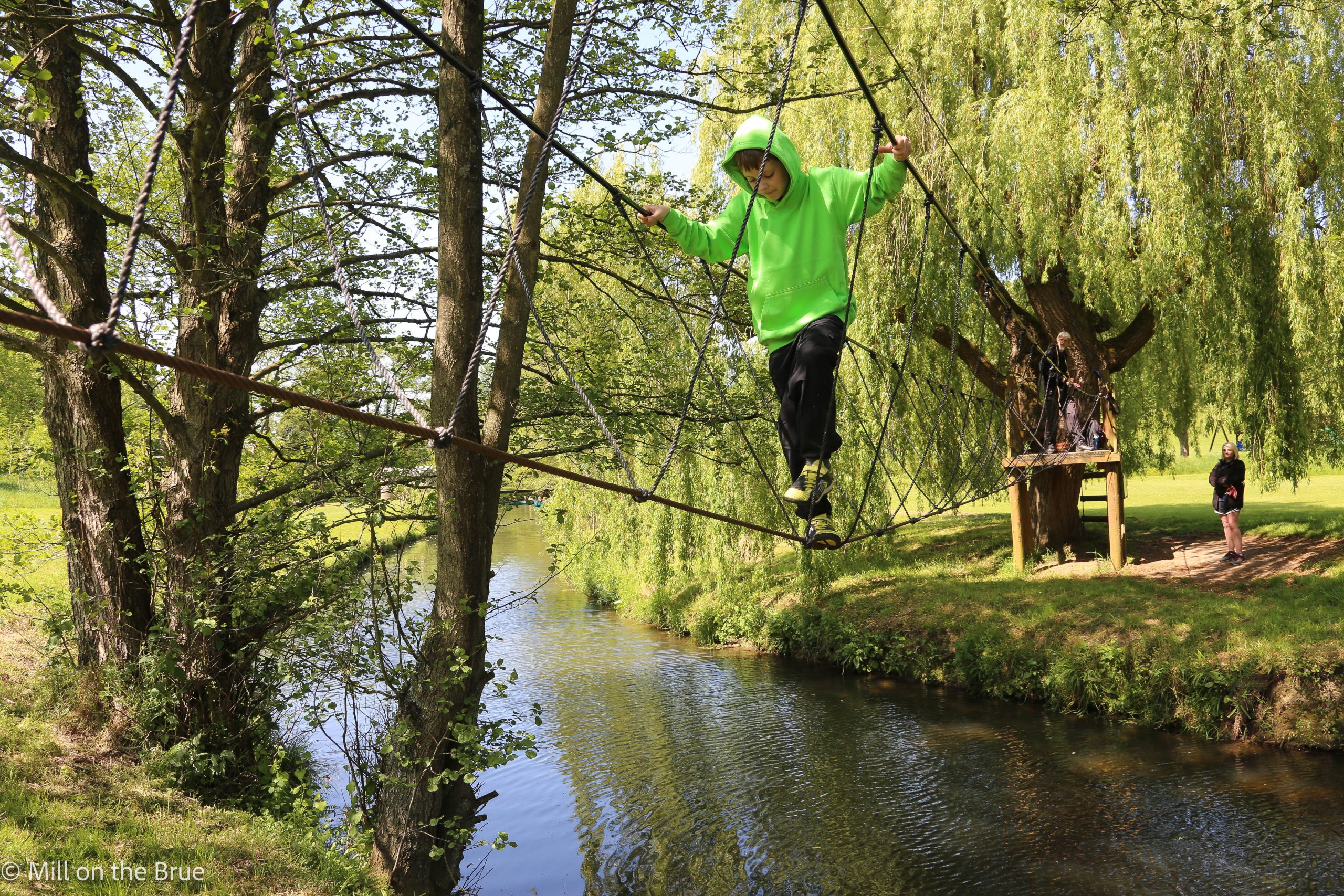 Child crosses a river on a rope bridge.