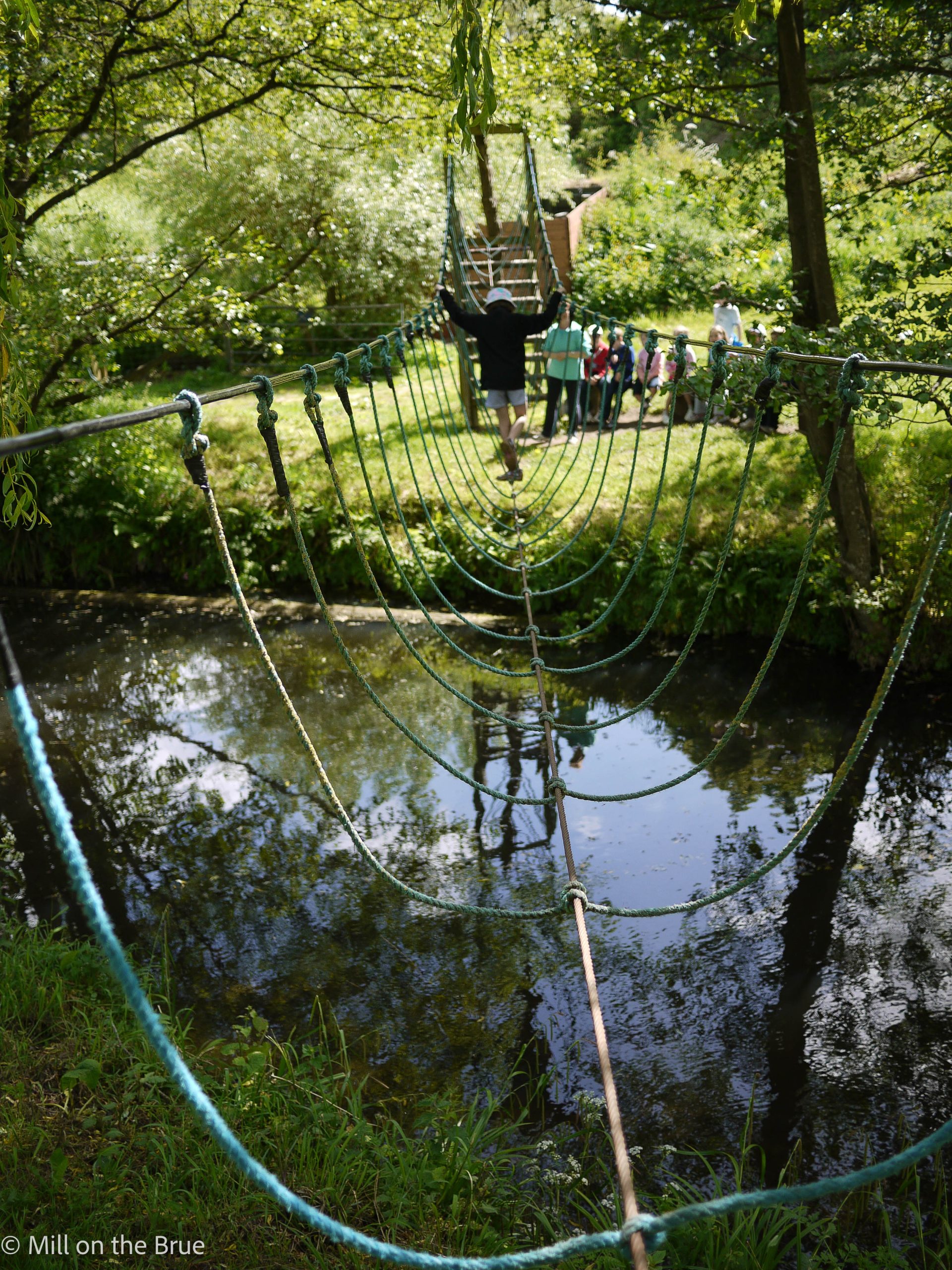 Child crosses a river on a rope bridge.