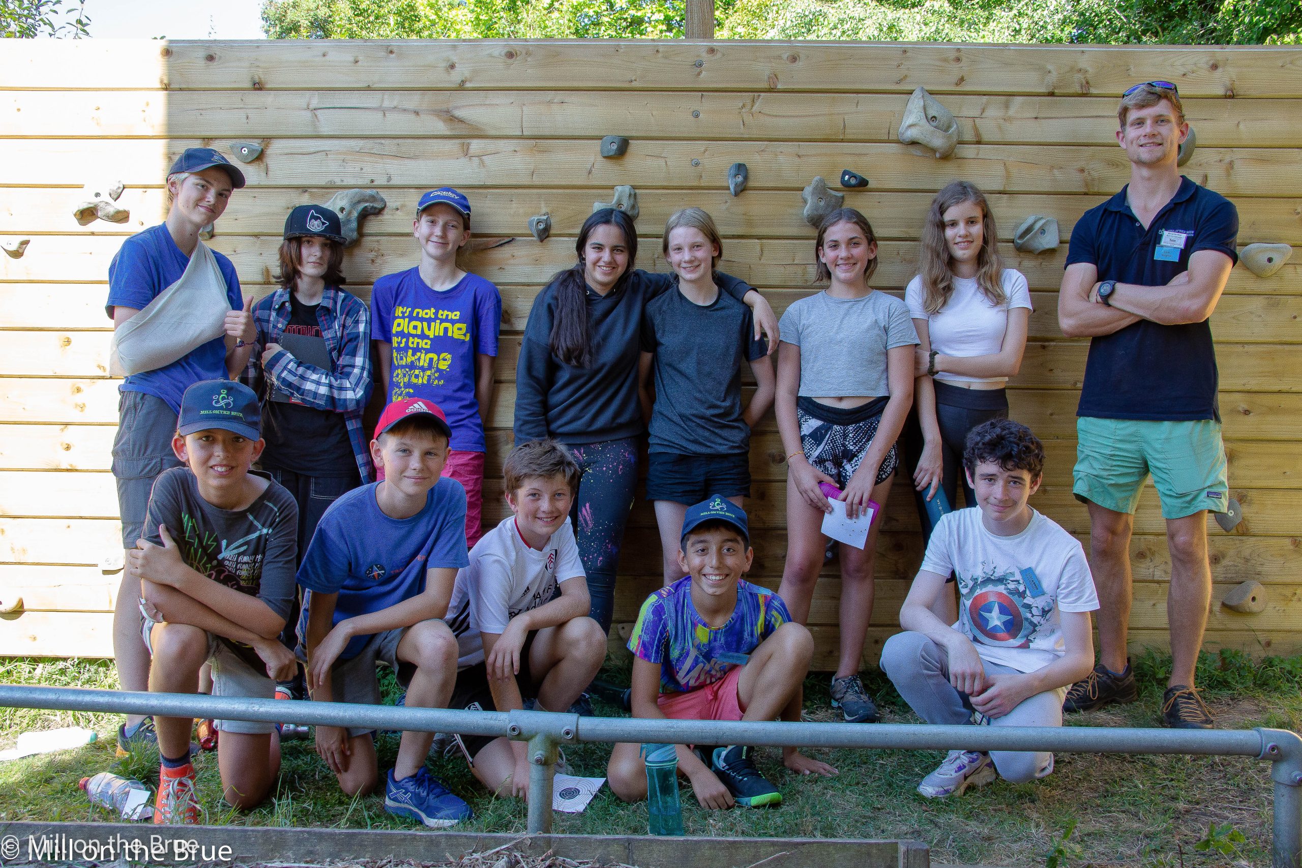 Students and instructor smile in front of a wooden climbing wall.
