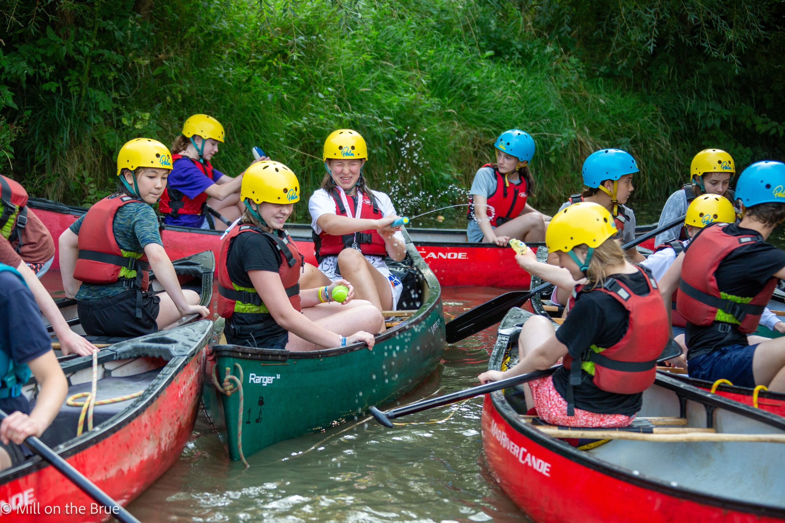 Teens play with waterguns in canoes.