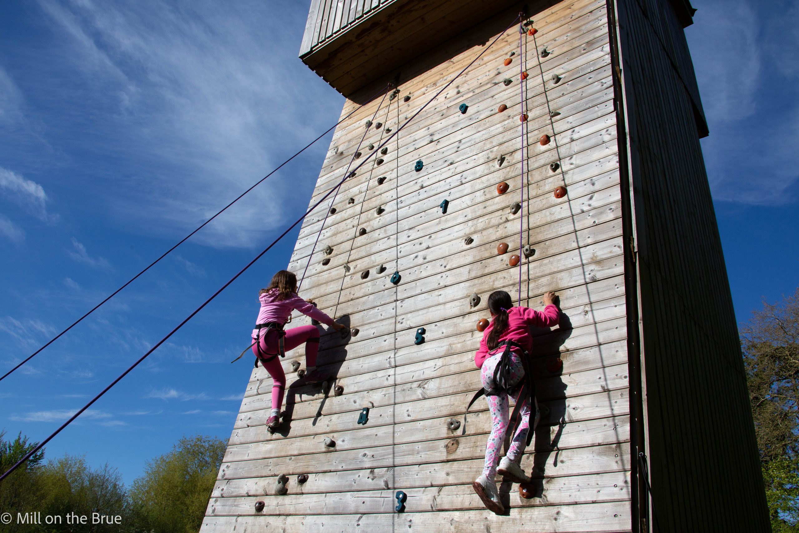 Children scaling a large wooden climbing wall.