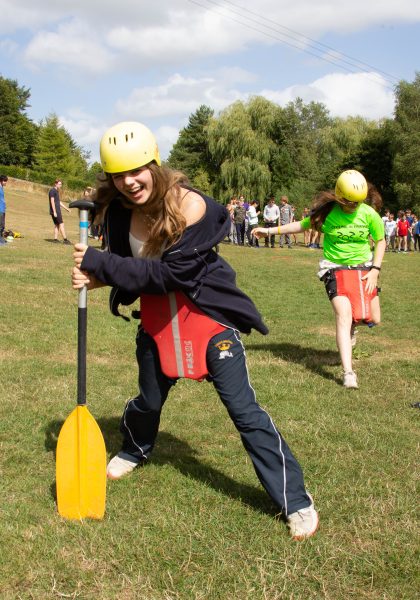 Students running and laughing with helmets, life vests on their legs, and paddles.