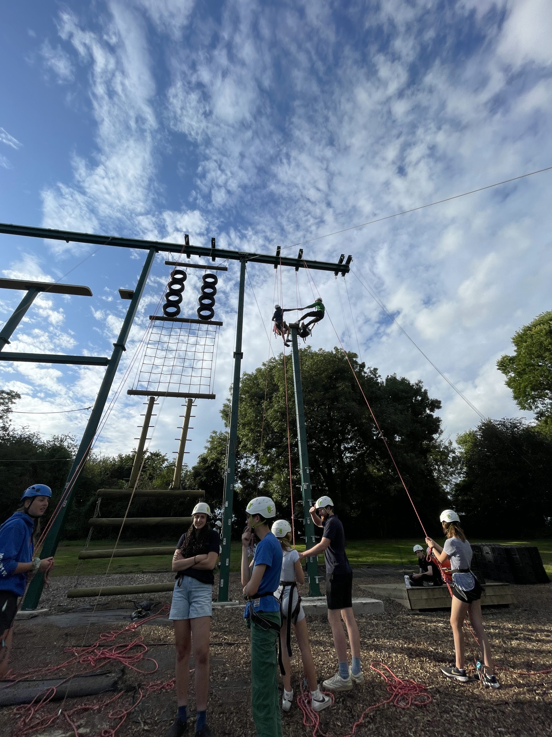 Students hold hands whilst suspended high in the air on ropes.