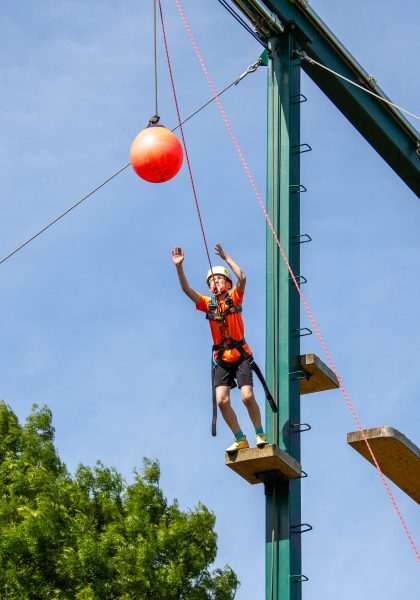 A student leaps through the air suspended on ropes.