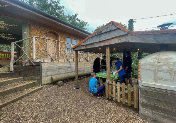 Instructor and students prepare to cook homemade pizza in an outdoor pizza oven.