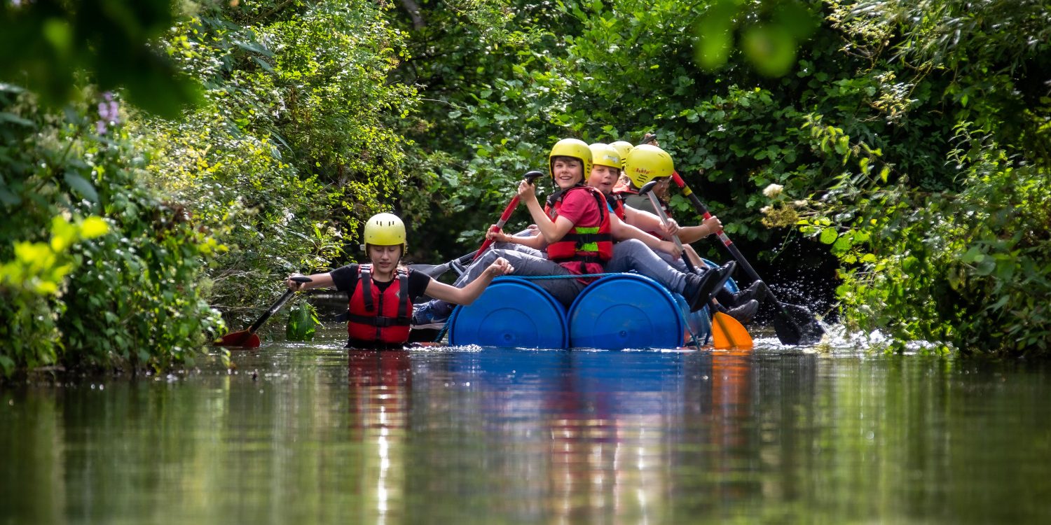 Students paddle on a raft made of barrels.