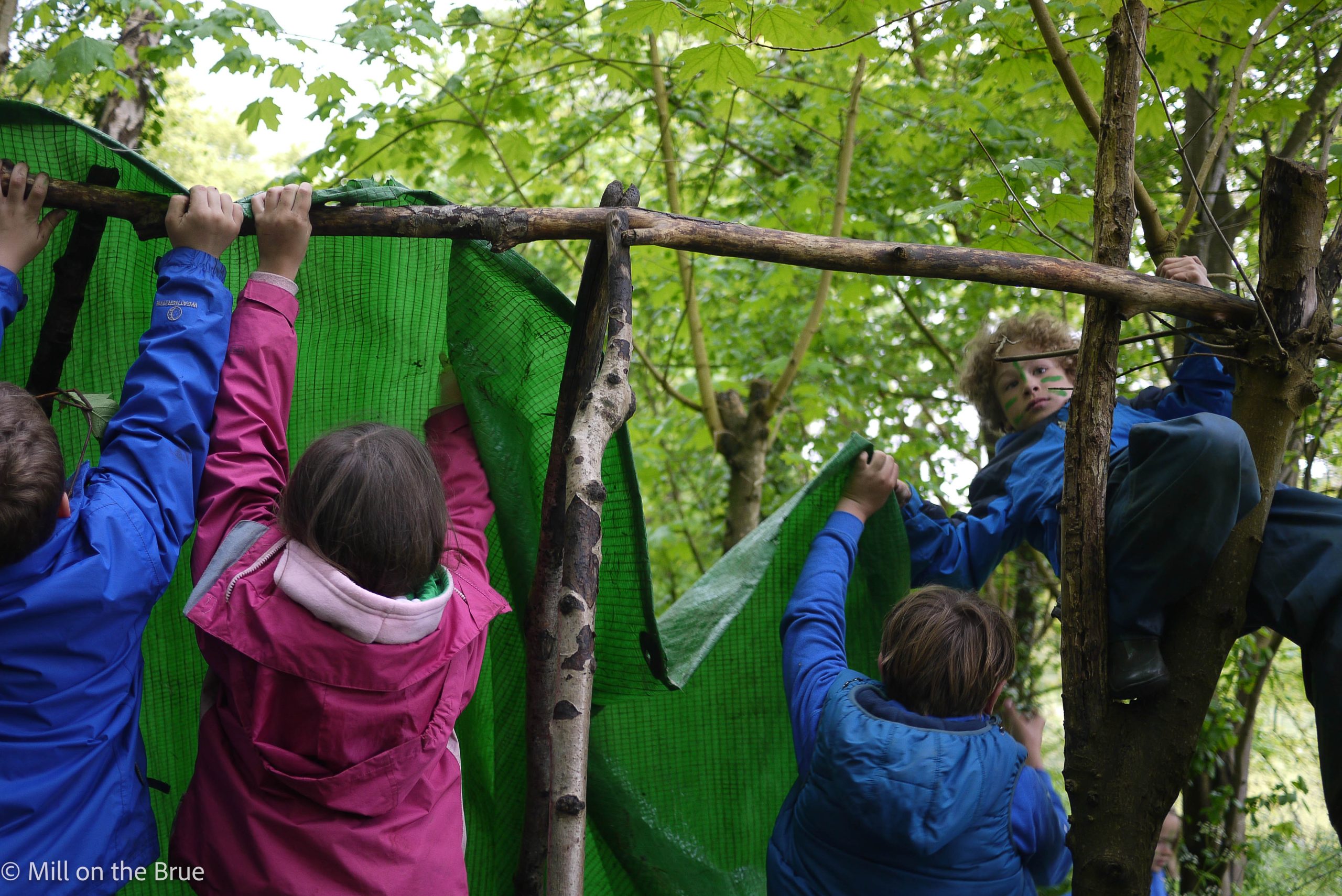 Children building a structure with tarps and branches.