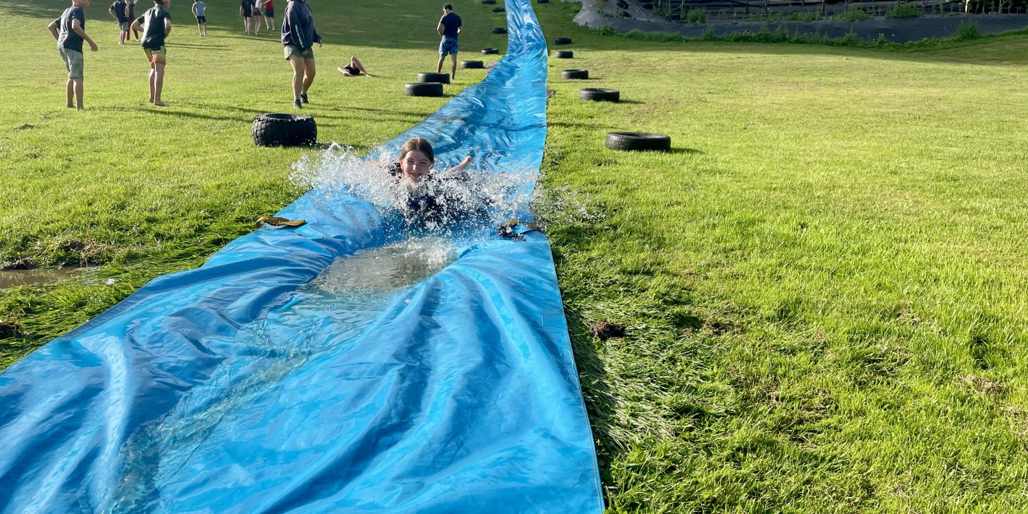 Child goes down a waterslide on a grassy hill.