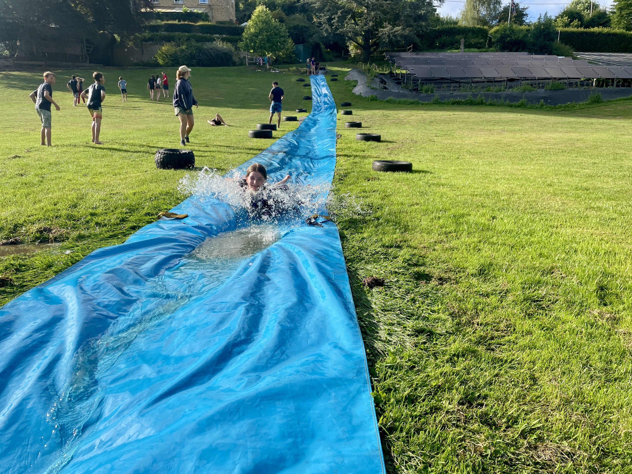 Child goes down a waterslide on a grassy hill.