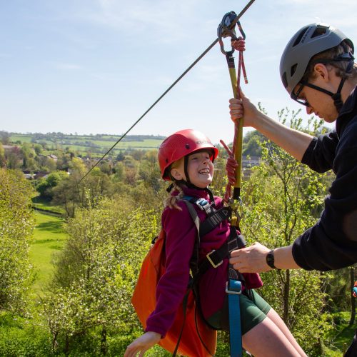 Instructor checks a child's safety harness before zip wire ride.